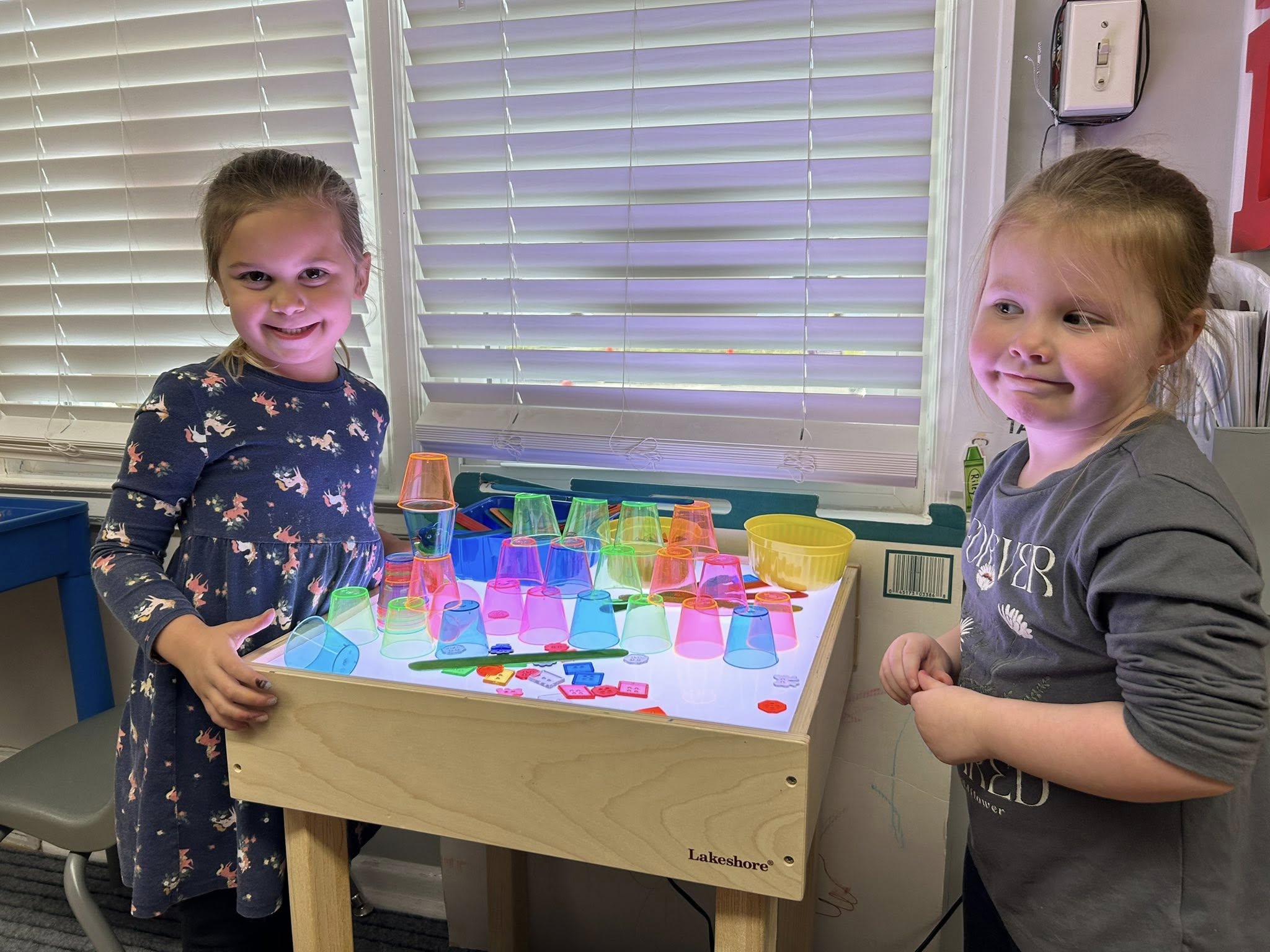 Two little girls playing at a standing table with blocks.