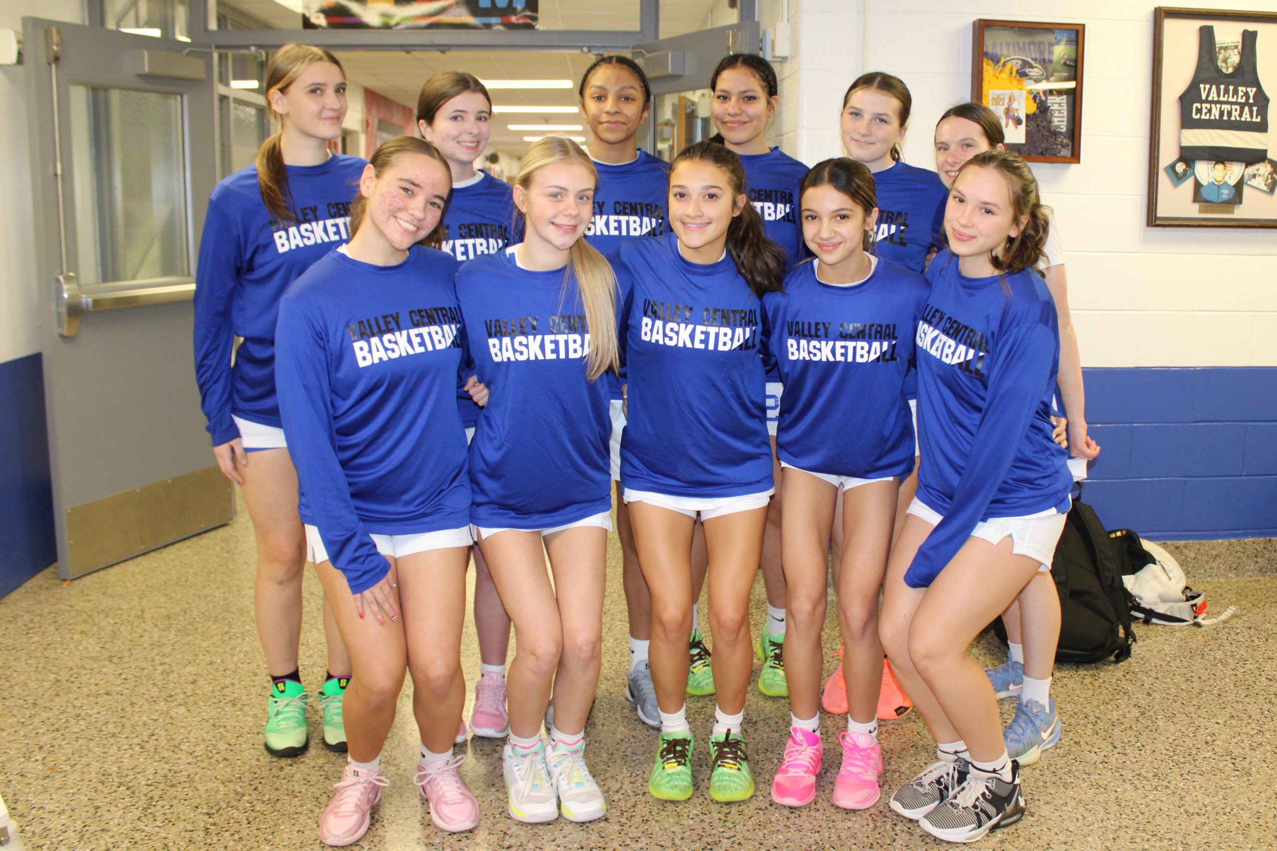 Girls varsity basketball players wearing matching blue shirts posing and smiling together.