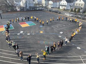 WES Staff on Upper Playground in yellow shirts standing in the shape of a heart (aerial photo) waving. 