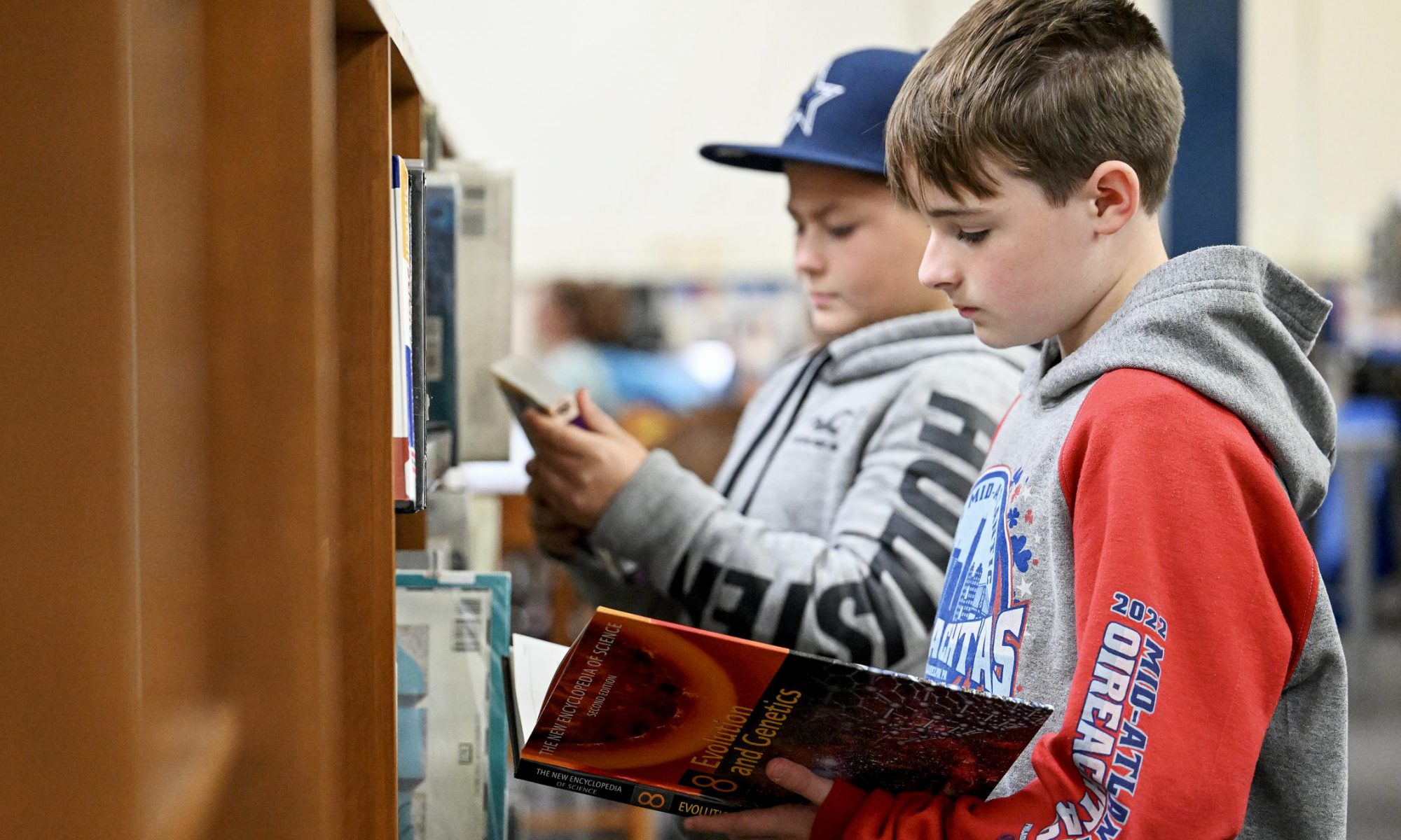Two Middle School students stand as they browse through books in the VCMS Library stacks.