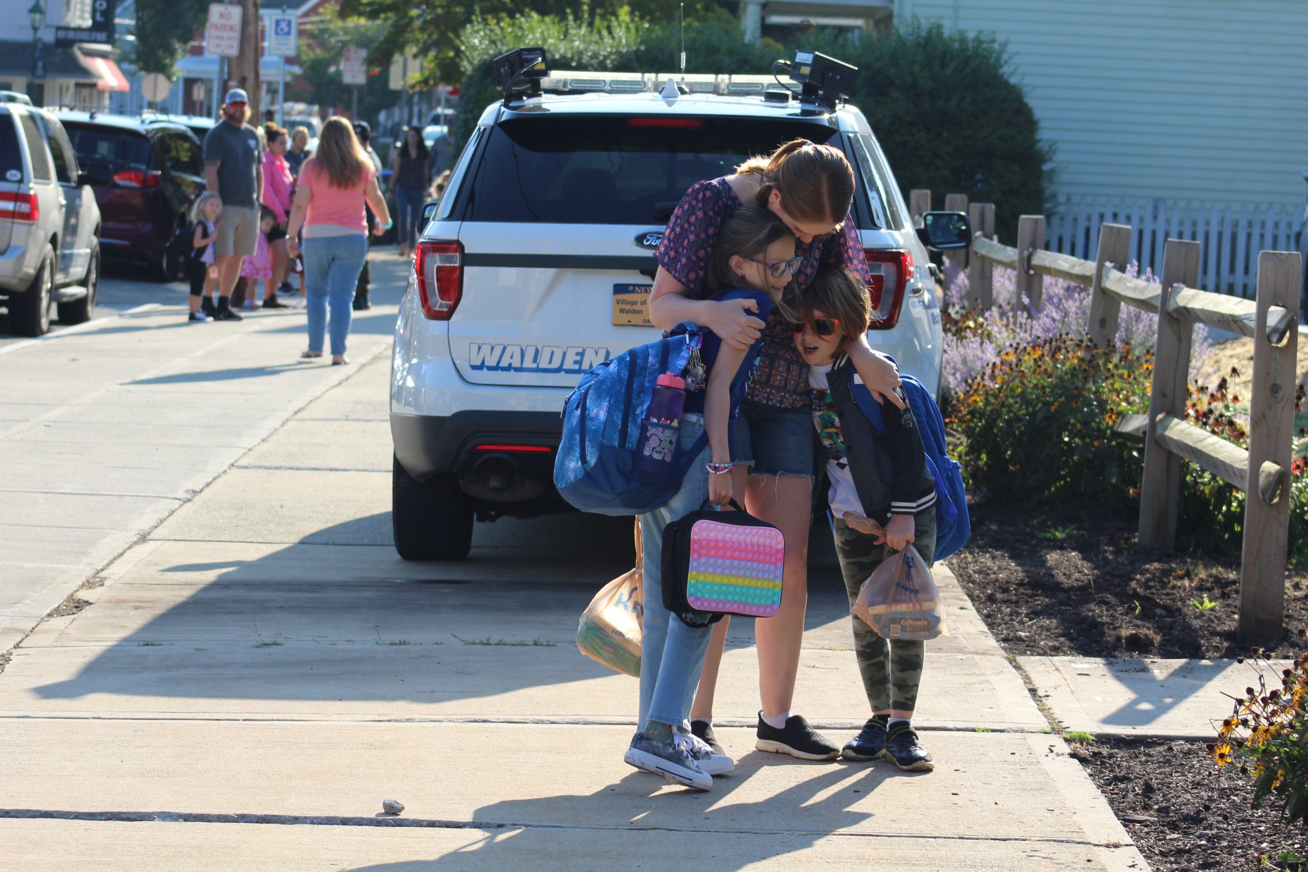 Two students hug a parent in front of the school on the first day of school. 