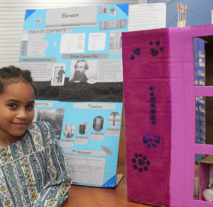 A student looks at the camera next to the diorama she created. 