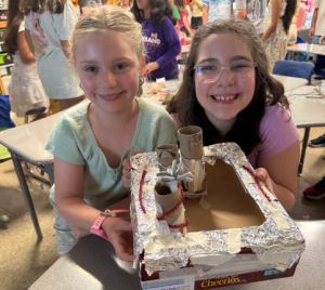 Two students show their creation to the camera as they smile for a photo. 
