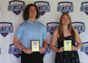 Two students hold up awards with their names on it and smile for a photo at the O.C.I.A.A. breakfast. 
