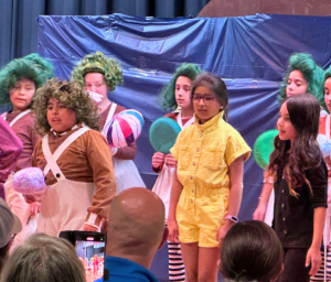 Students stand and sing during a performance of Willy Wonka. 