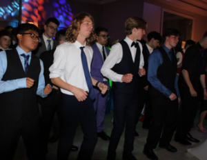 Students dancing at the senior ball in suits in a dark room at the event. 