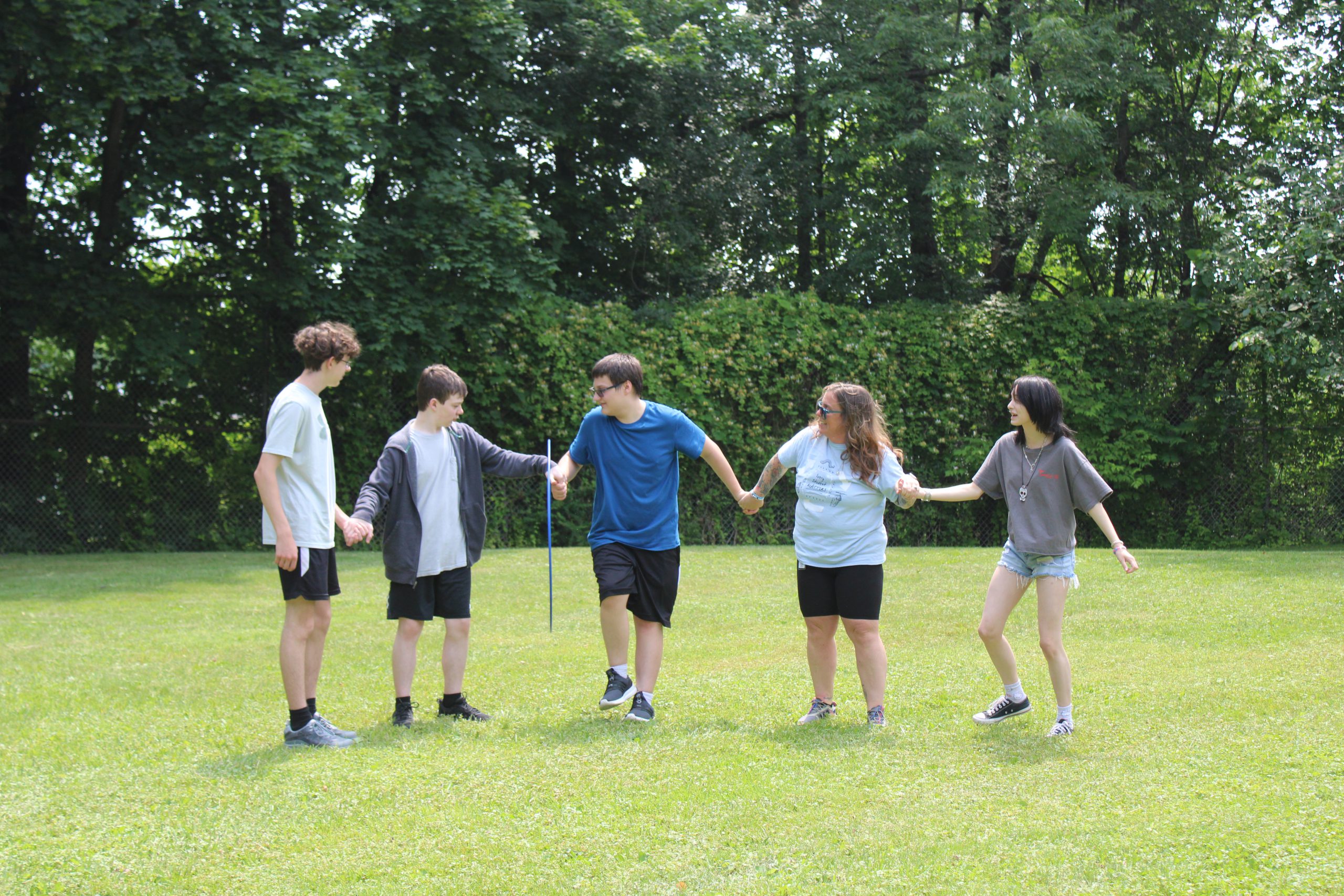 Five people stand in a field with a hoola hoop and move it over their bodies during field day. 
