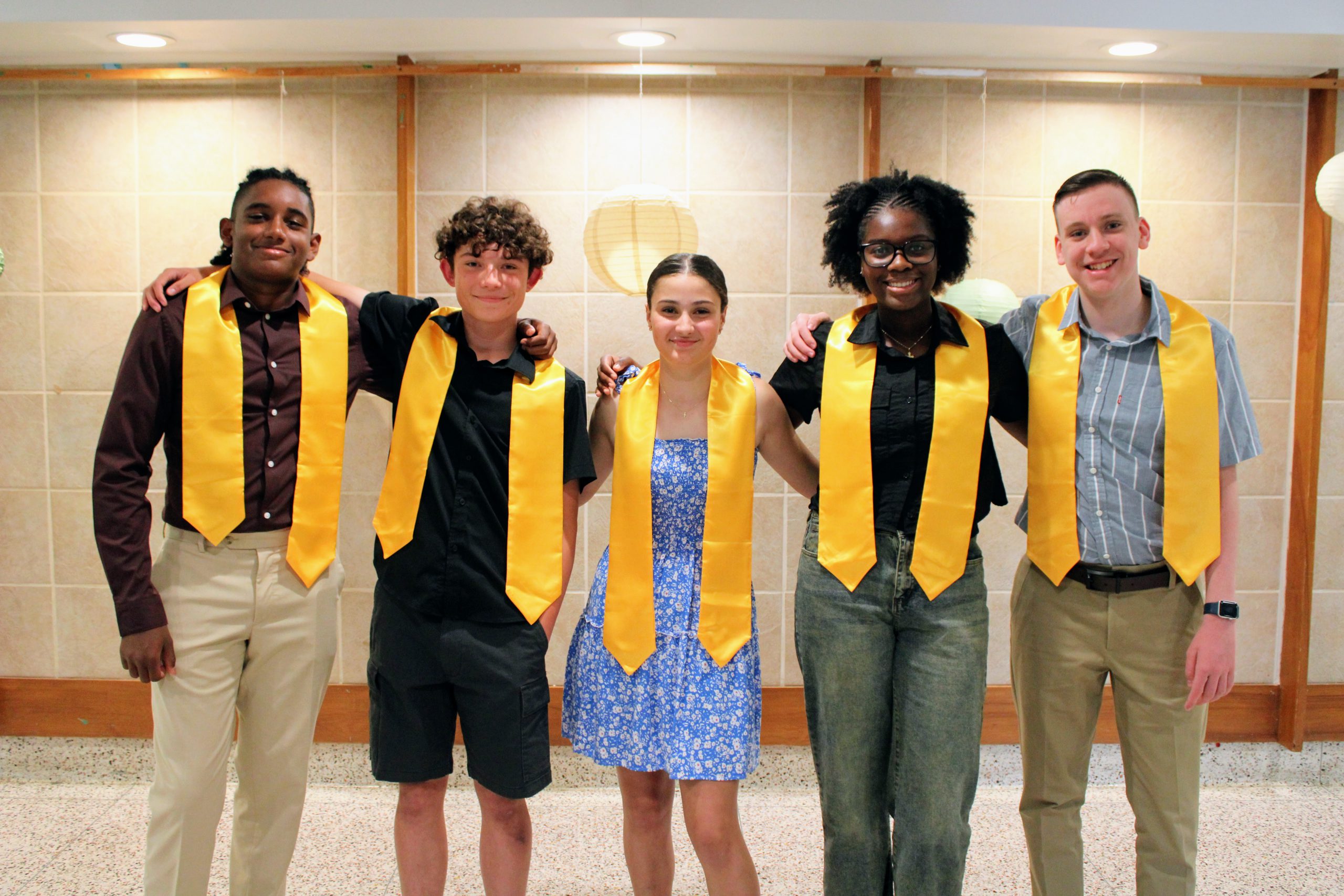 Five students stand next to each other in their sashes at their eighth grade moving up ceremony. 