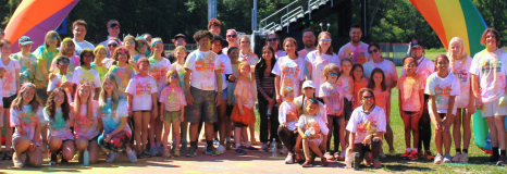 Group of people posing under a rainbow balloon arch.