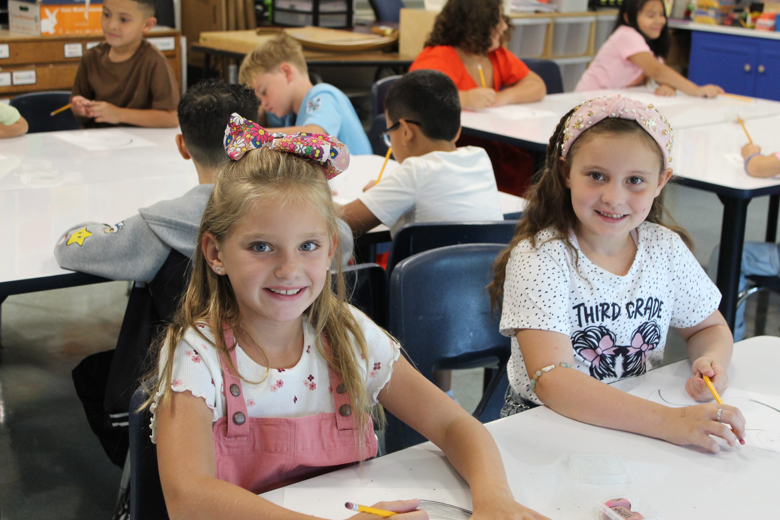 Two girls smile for a photo while sitting at a table on the first day of school. 