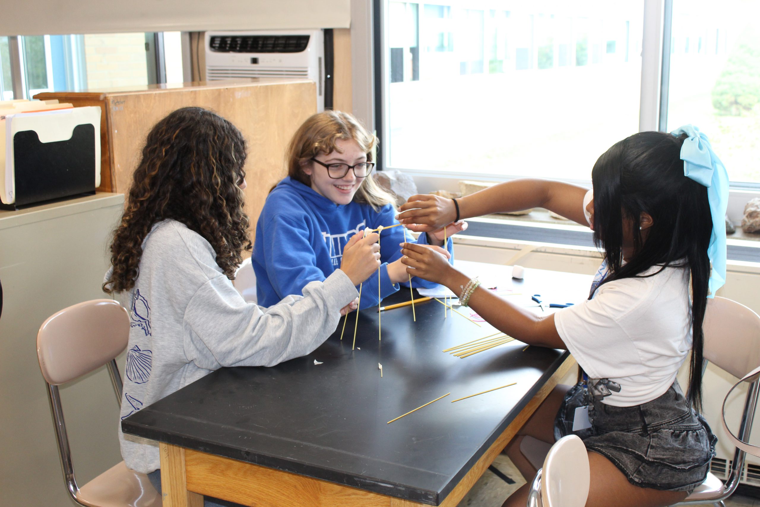 Three students work on a project in a classroom and smile. 