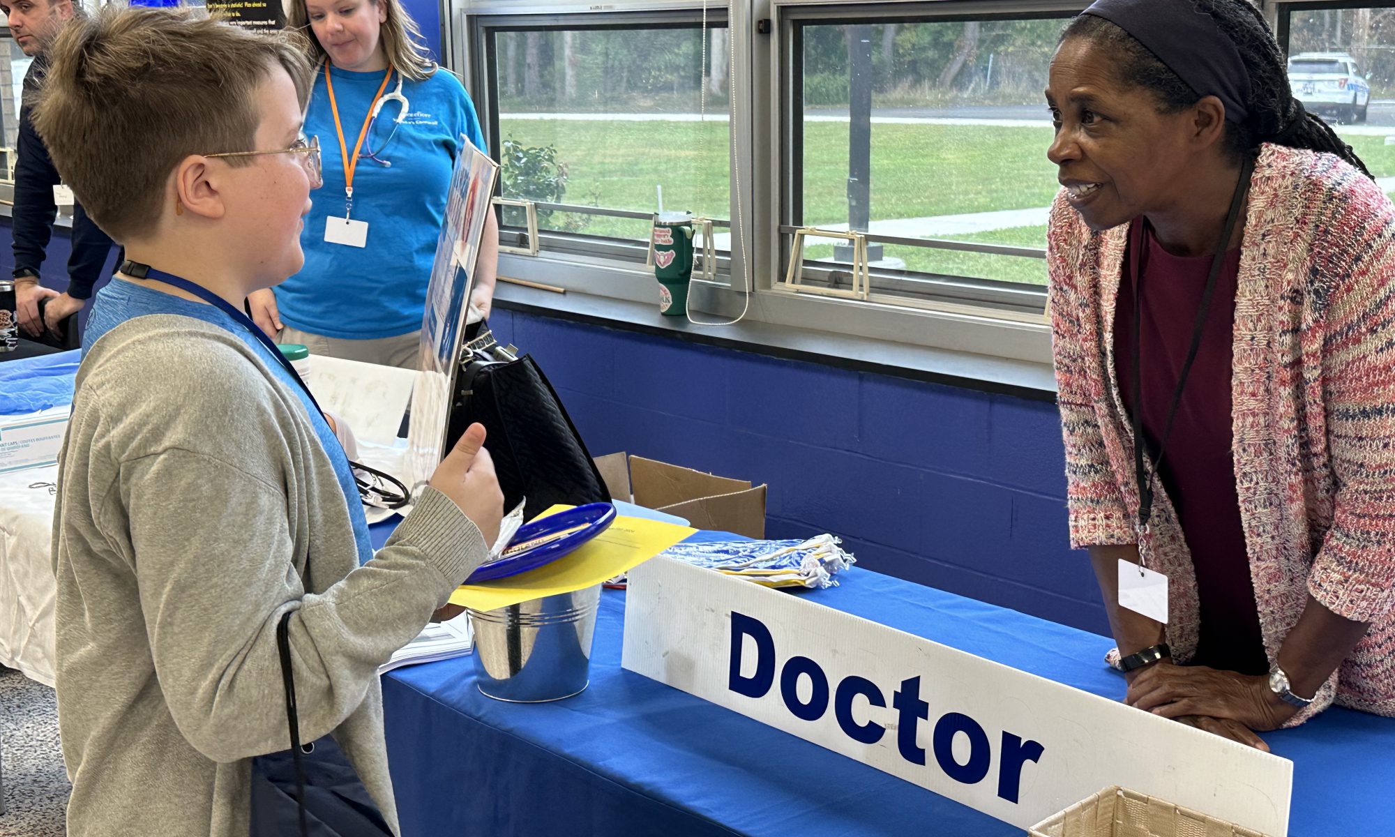 Boy talking to a woman at a table with a sign on it that says Doctor.
