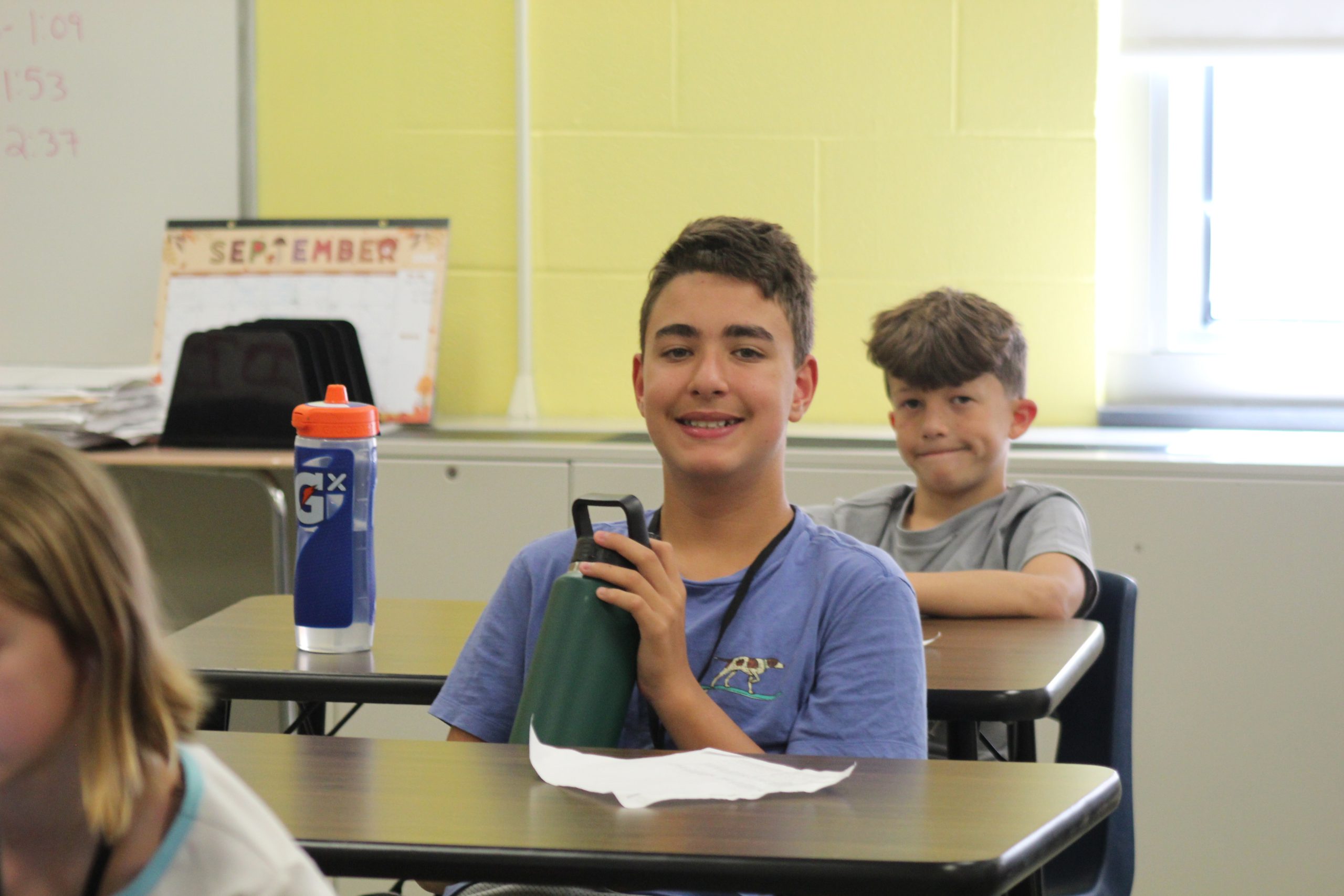 A student smiles for a photo at a desk on the first day of school. 