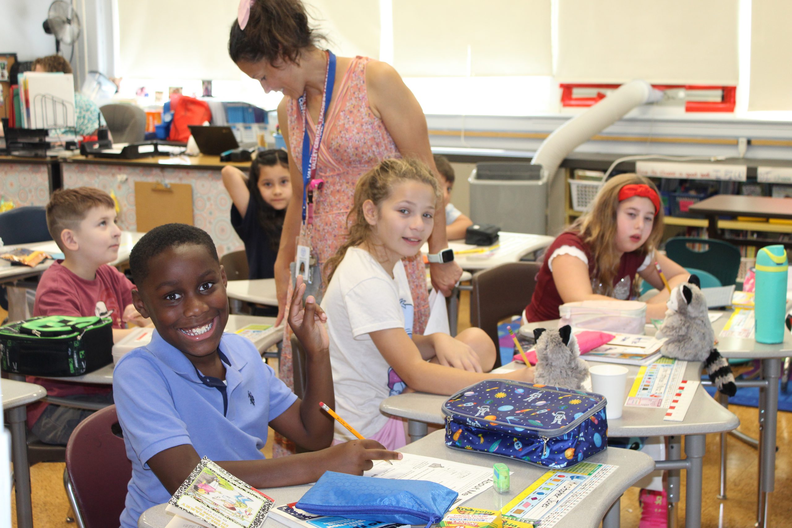 Six students working on an assignment at their desks and a teacher checking a students work in the second row of desks.