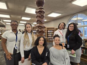 Group of students in a library posing next to a totem statue.