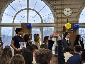Students lined up near a podium in front of a crowd of other students.