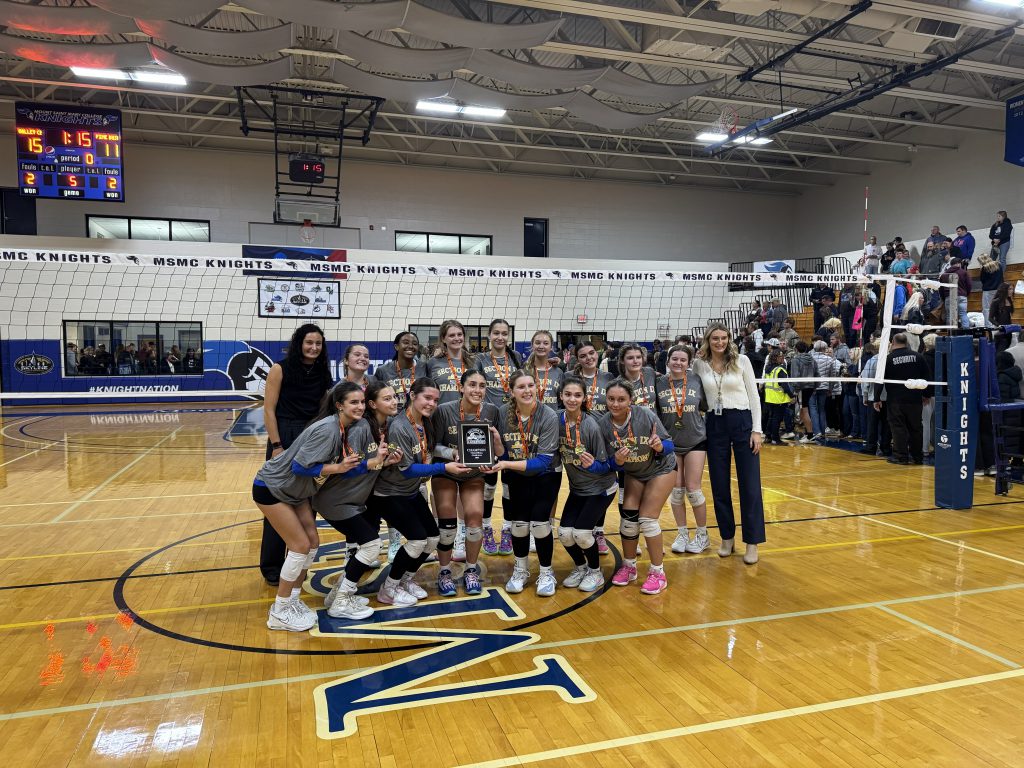 girls varsity volleyball team posing with their sectionals plaque on the volleyball court.