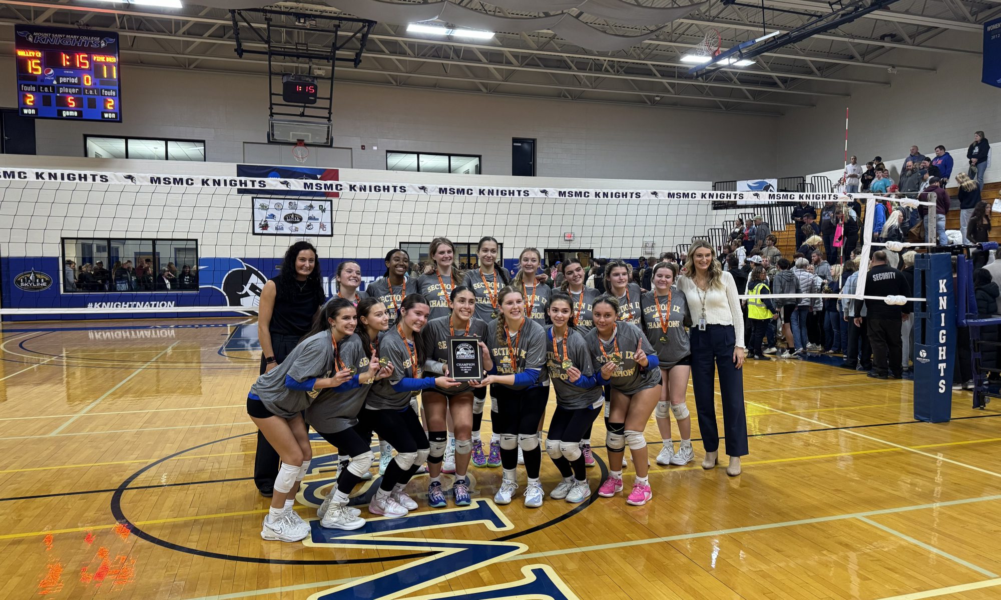 girls varsity volleyball team posing with their sectionals plaque on the volleyball court.