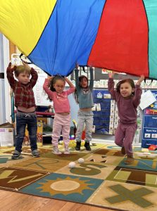Four pre-k students playing with a parachute.