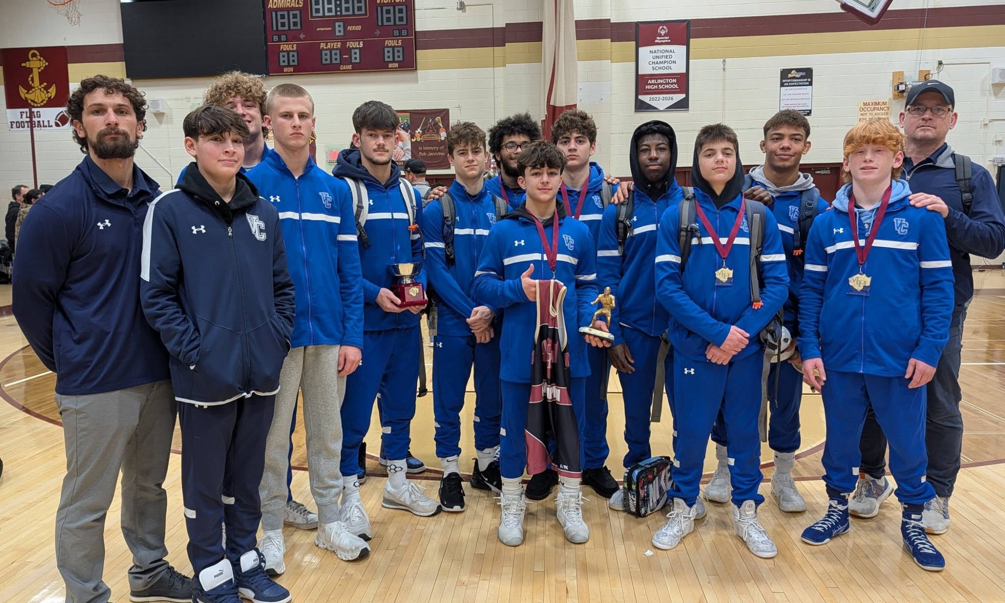 VC Varsity Boys Wrestling team posing with their coaches.