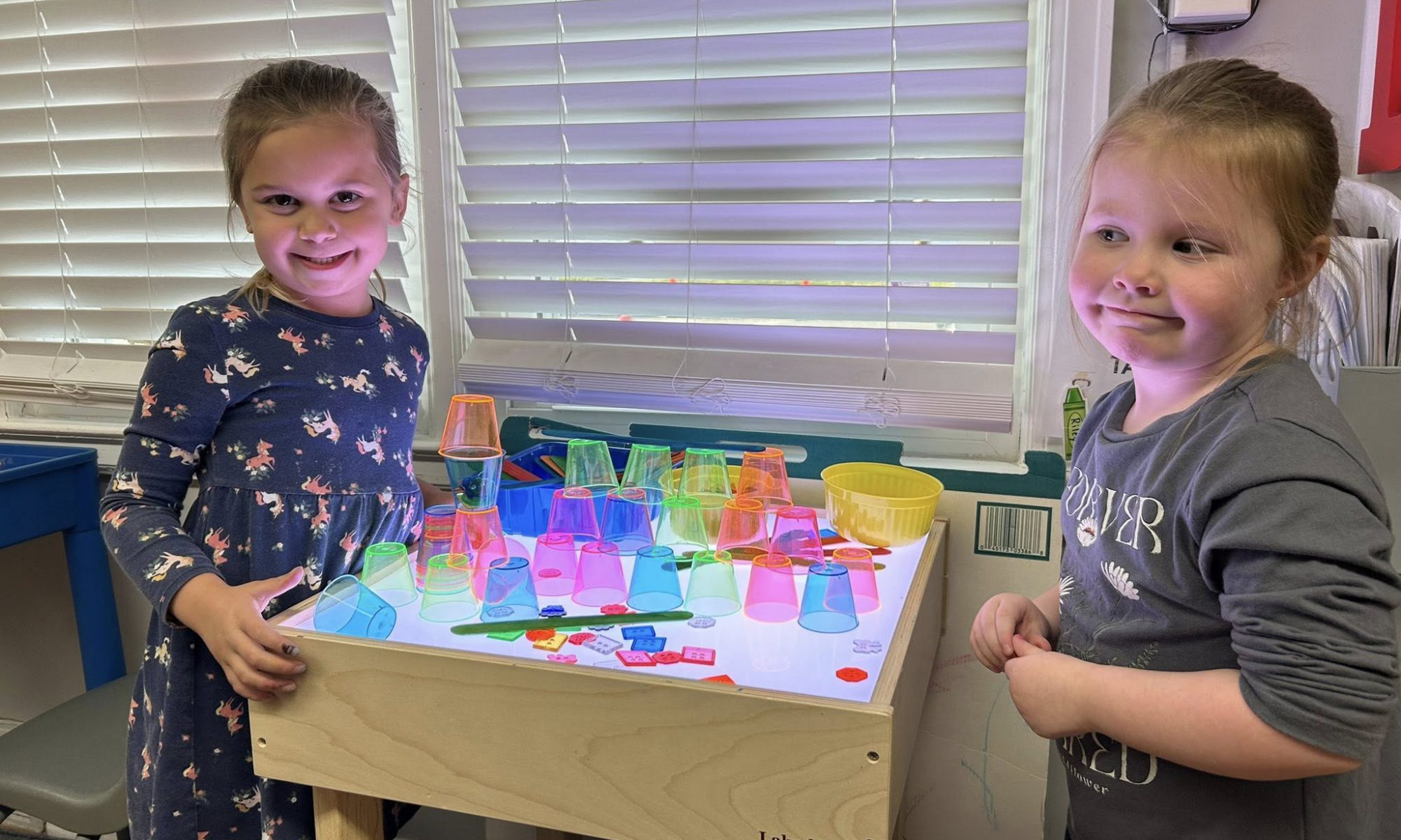 Two little girls playing at a standing table with blocks.