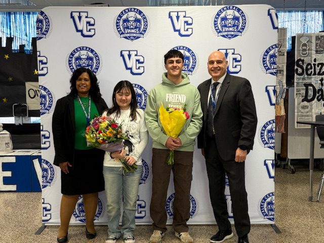 Class of 2026 Valedictorian Michael Catania, Jr. and the Salutatorian Susan Kirk holding bouquets of flowers in front of a step and repeat banner with Valley Central School District's logos on it. Standing on either side of them is Superintendent Evette Avila and the VCHS interim principal Louis Adipietro.