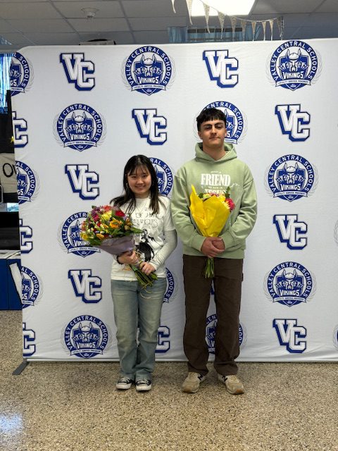 Class of 2026 Valedictorian Michael Catania, Jr. and the Salutatorian Susan Kirk holding bouquets of flowers in front of a step and repeat banner with Valley Central School District's logos on it.