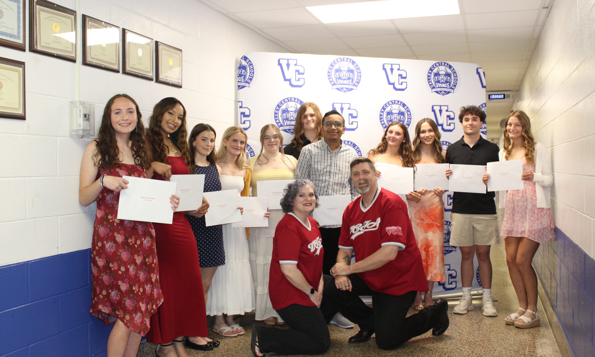 Bunch of students holding scholarship certificates and two teachers squatting in front.