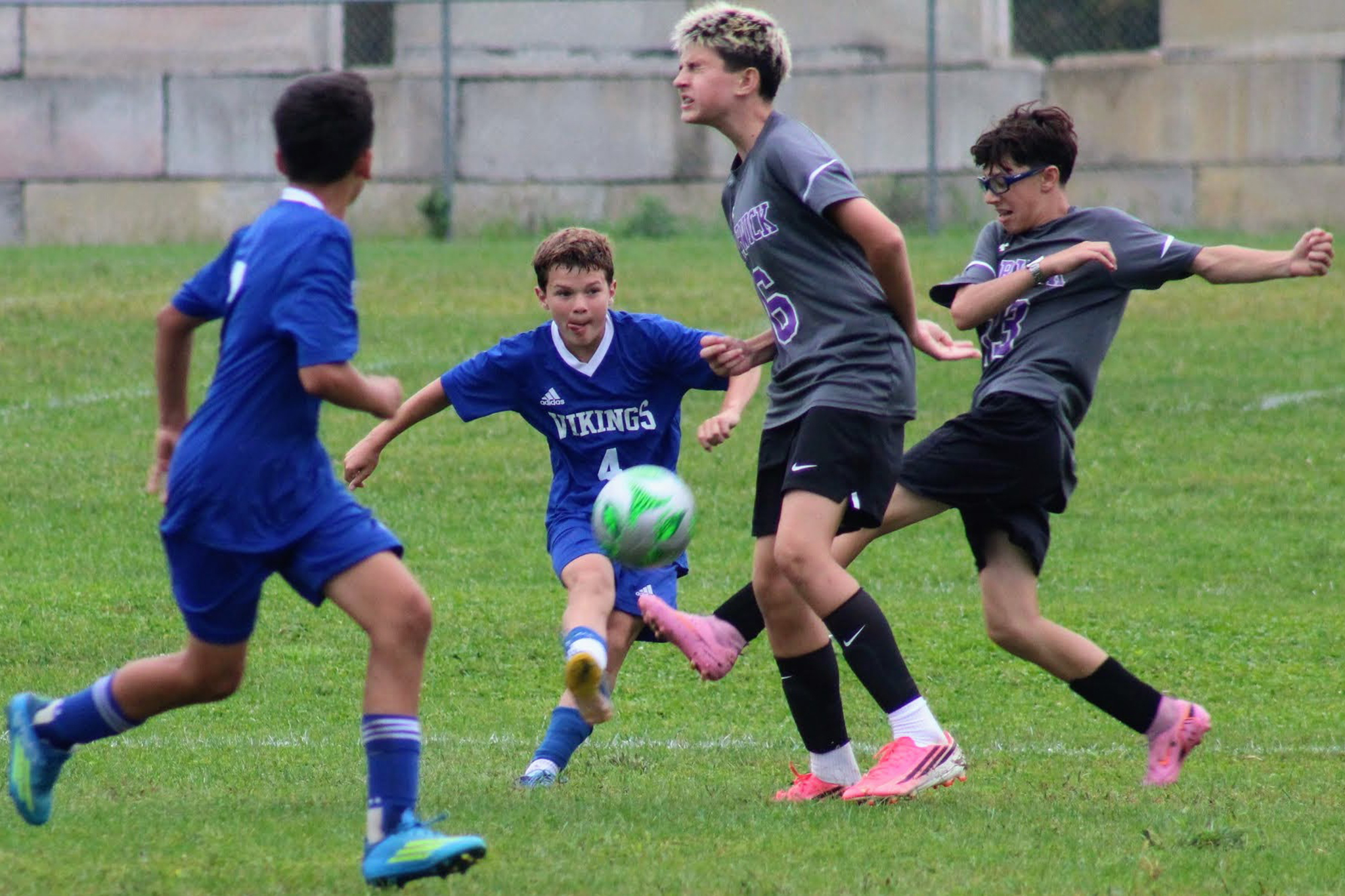 Two opposing soccer players go for the ball after another player stopped it and a teammate waits for a pass