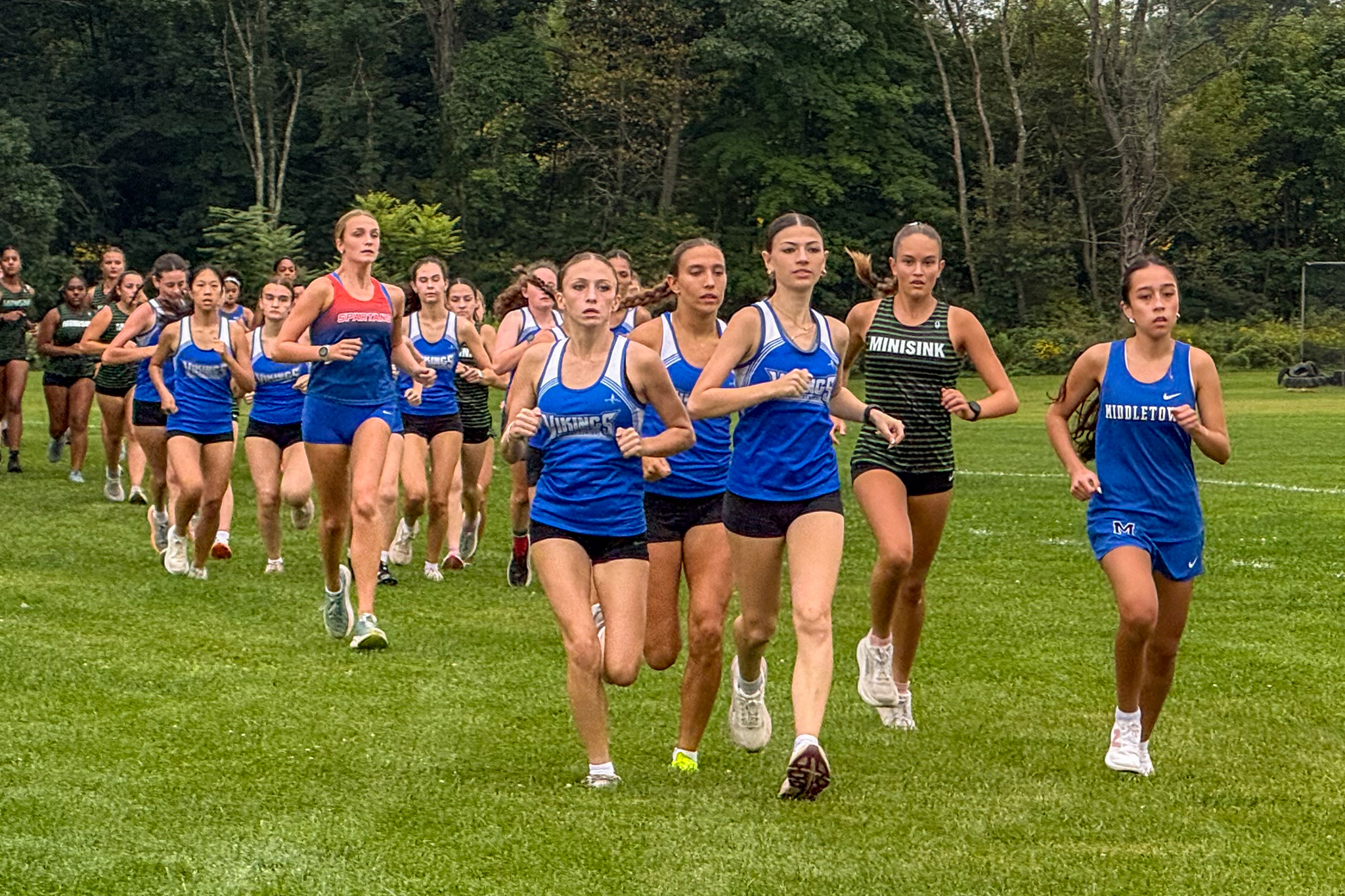 Cross country runners start a girls race en masse at across a field.