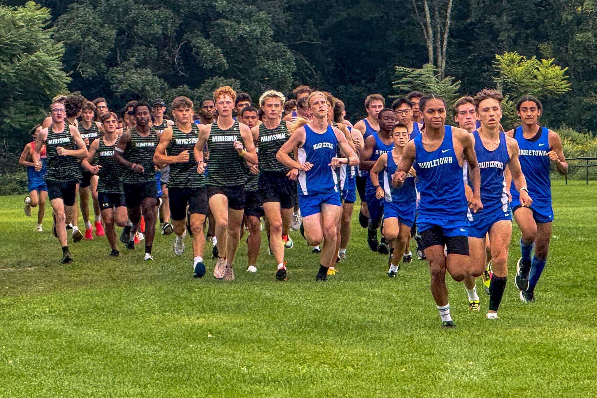 Cross country runners start a boys race en masse at across a field.