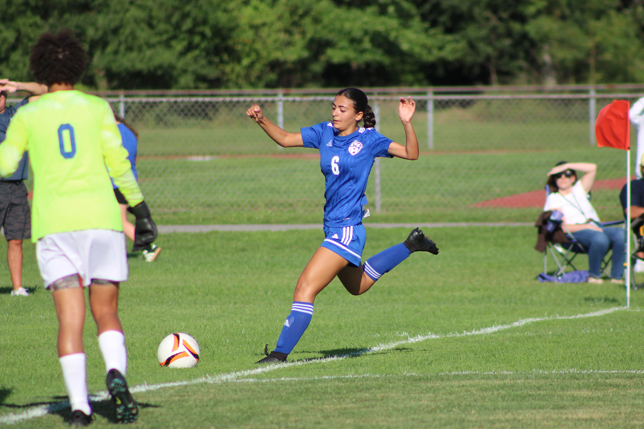 A soccer player chases the ball over the end line as a goalie watches