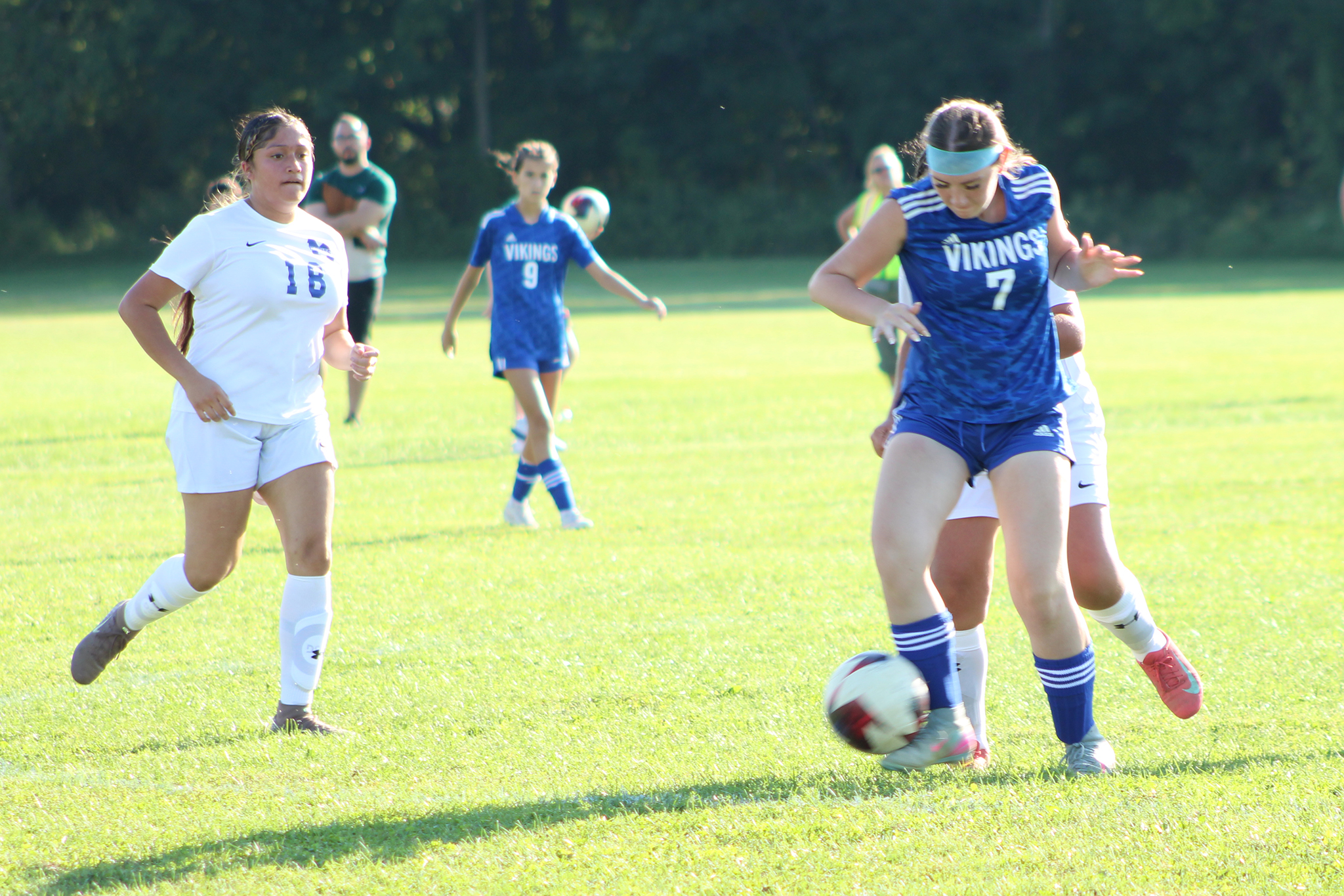 A soccer player controls the ball as opponents approach from behind and the side and a teammate watches