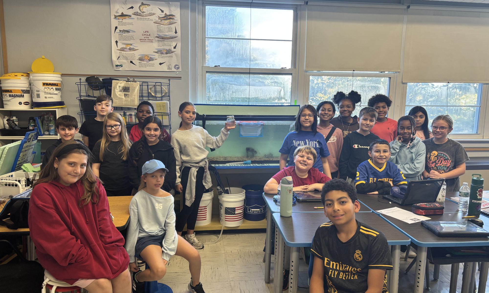 Students pose in a classroom with a trout fish tank